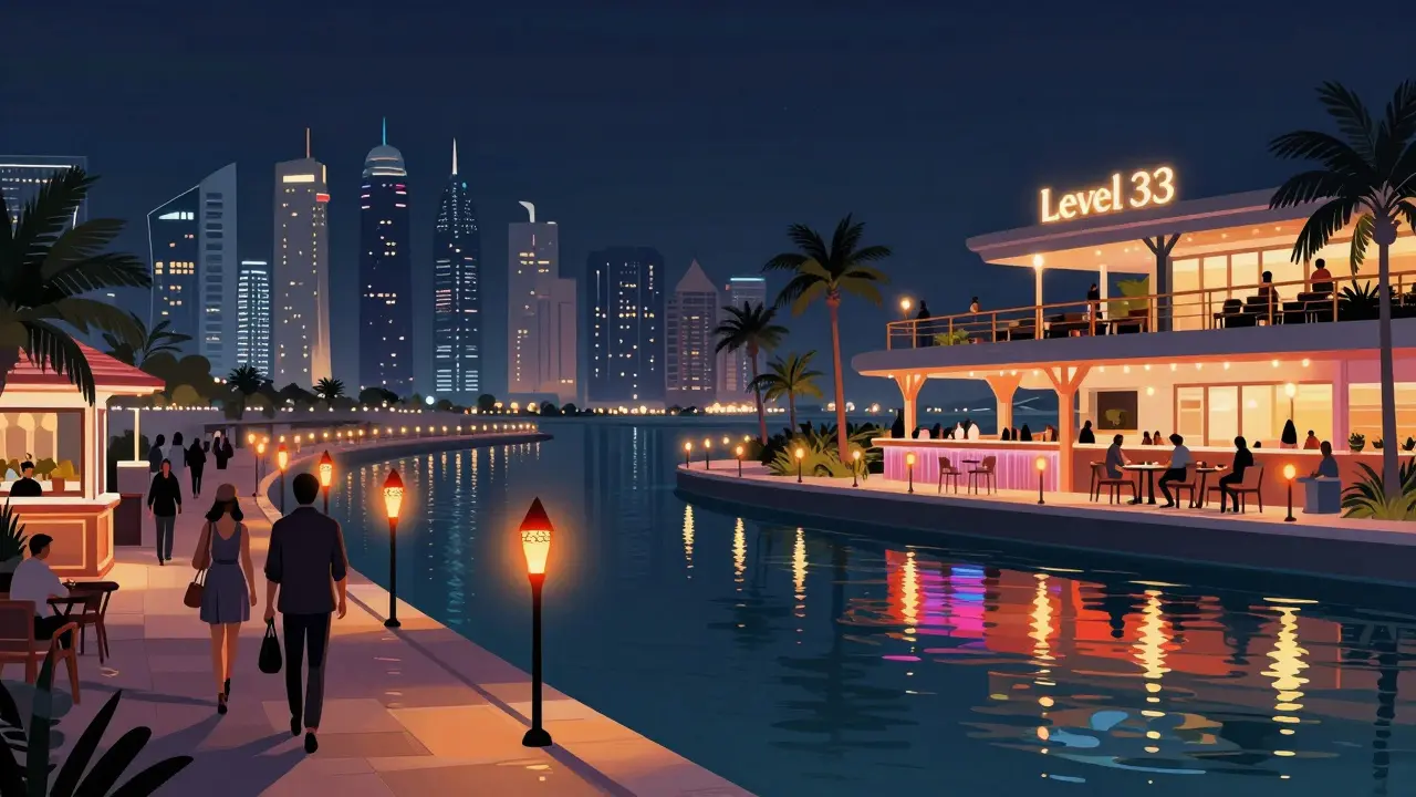 Waterfront promenade with glowing bars and reflections on canal, city skyline in distance.